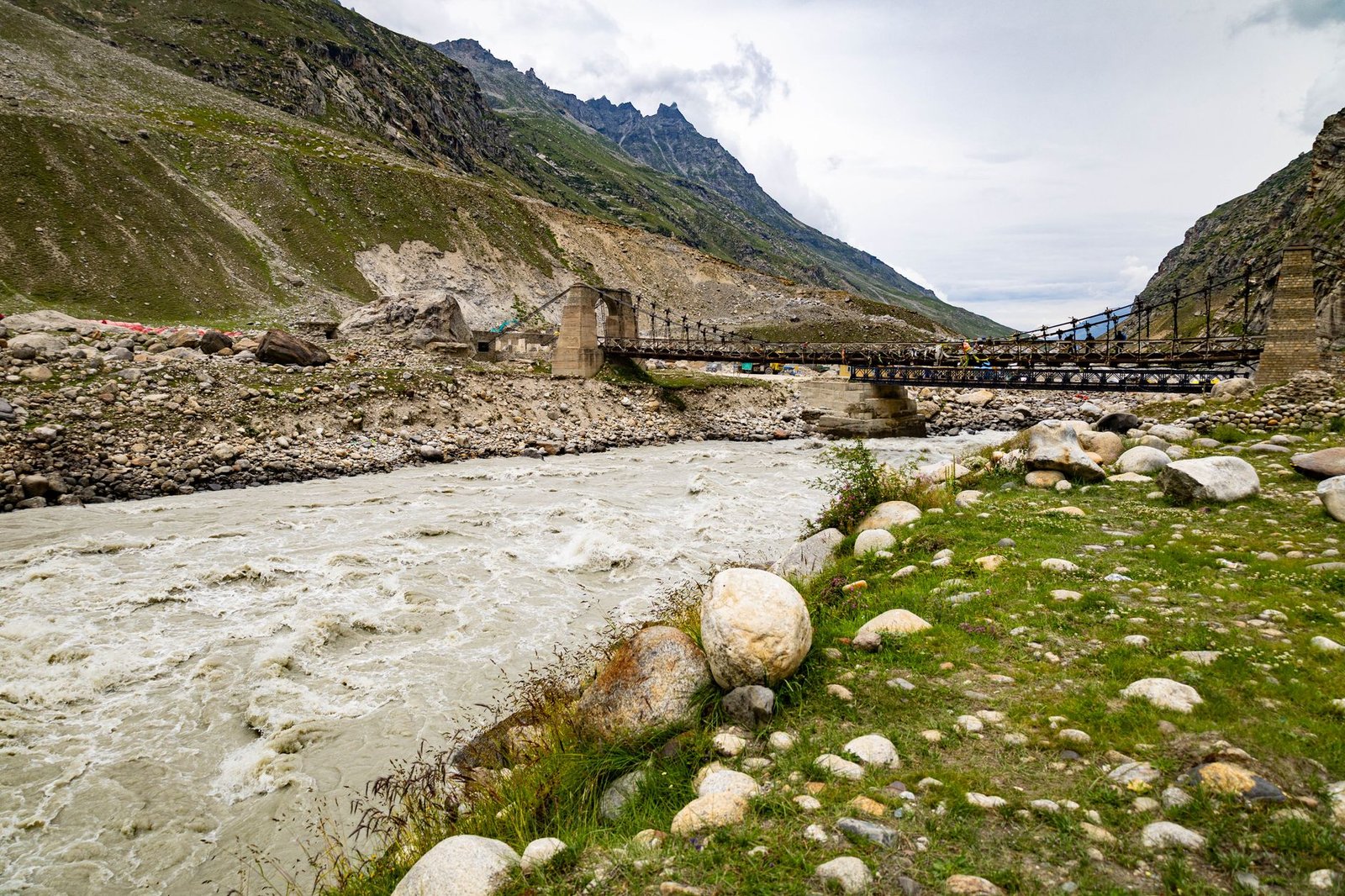 Picturesque view of a rocky river and suspension bridge amidst the Himalayan mountains.