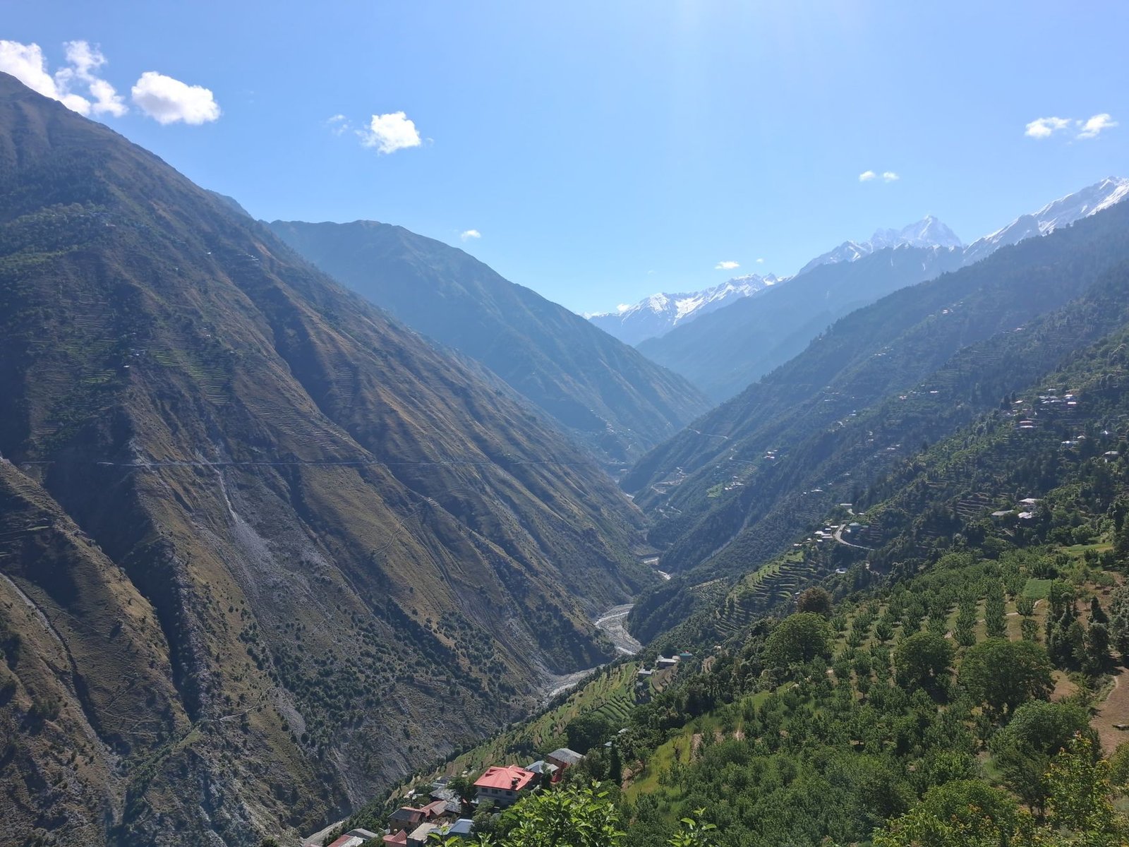 A breathtaking view of a lush green valley in the Himalayan mountains under a clear blue sky.