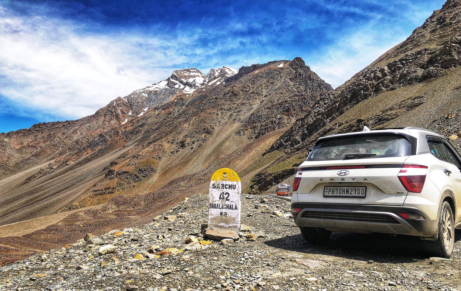 A white SUV on a rugged mountain road with a distance marker in the Himalayas.