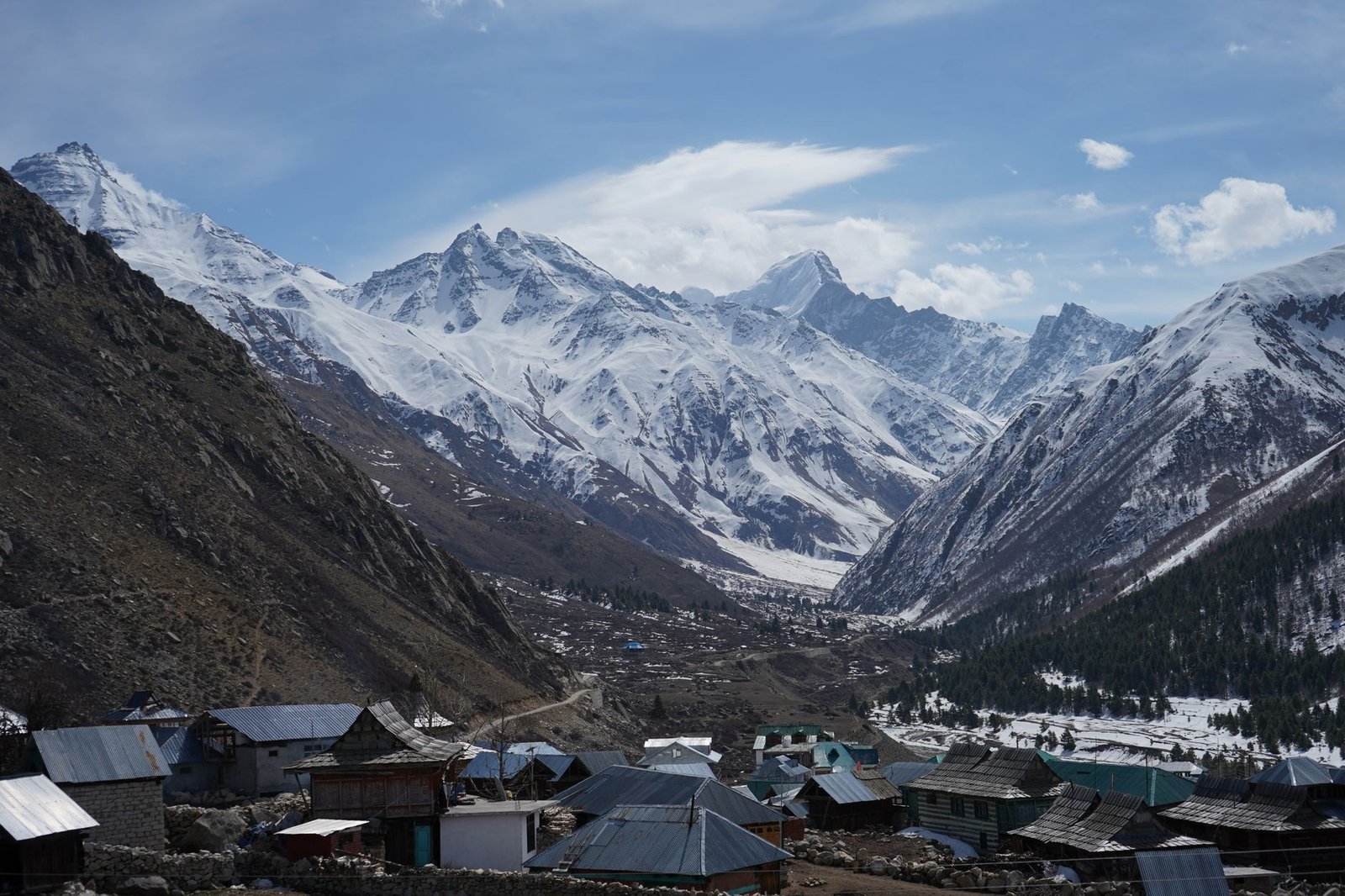 Breathtaking view of a Himalayan village surrounded by towering snow-capped peaks under a clear blue sky.
