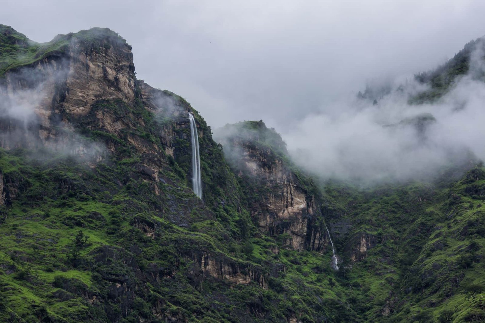 Breathtaking view of a waterfall cascading down misty green mountains in Himachal Pradesh, India.