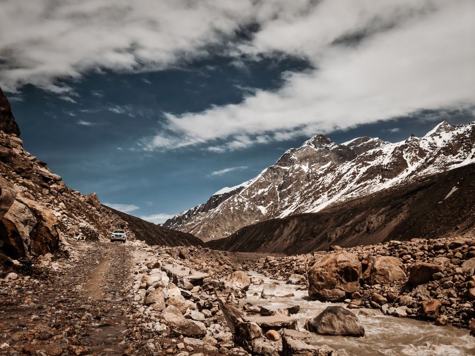 Off-road vehicle driving through the rocky and scenic Marango Rangarik landscape, surrounded by snow-capped mountains.