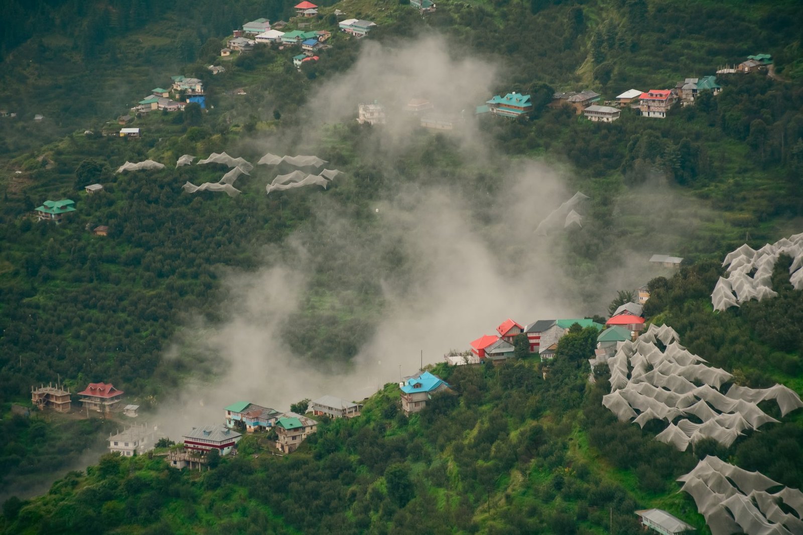 Scenic aerial view of a mist-covered village nestled in Himachal Pradesh, India, surrounded by lush greenery.